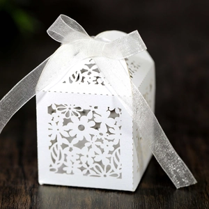 Detail of white laser-cut floral candy box with elegant organza ribbon on wood background