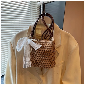 Détail du sac seau en paille tissée avec nœud en dentelle et chaîne de perles élégante