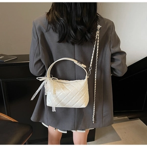 White quilted shoulder bag with lace bow and pearl charm shown on model in grey blazer