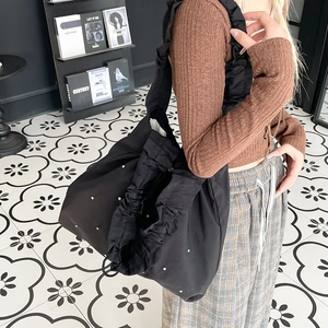 Detail of black nylon tote bag featuring ruffle shoulder strap and pearl embellishments