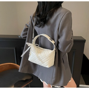 Detail showing white quilted pillow bag with pearls, ribbon bow, and chain strap