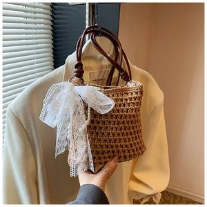 Gros plan d'un sac en paille avec un grand nœud en dentelle blanche et un charm en perles