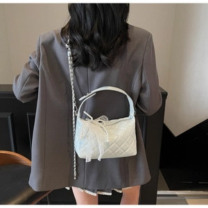 Detail of light blue quilted leather bag with lace bow and pearl charm on shoulder