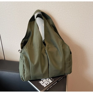 Army green large nylon tote bag with pleated design resting against a textured wall