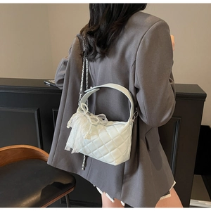 Close-up of white quilted handbag featuring lace bow and pearl chain details