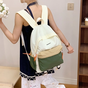 Three-color nylon backpack detail featuring cream, khaki, and dark green panels with orange drawstring
