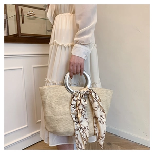 Close-up of beige woven straw tote with silver metal ring handle and decorative silk scarf