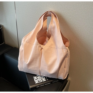 Détail du sac cabas plissé rose clair en tissu haute densité sur un banc en cuir noir