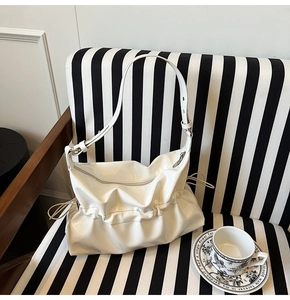 Détail du sac hobo blanc plissé en cuir brillant sur un canapé rayé avec café