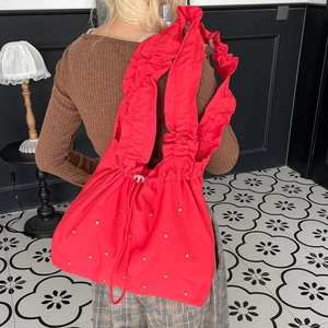 Detail of red nylon tote bag with ruffled straps and silver rhinestones shown on model