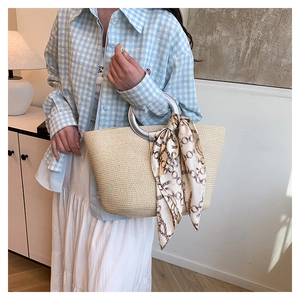 Detail of woven straw tote bag featuring silver metal handles and a decorative silk scarf
