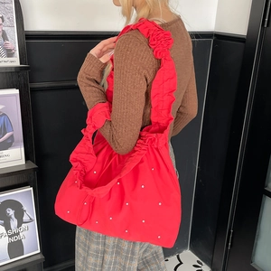 Detail of red nylon tote bag featuring ruffled strap and sparkling rhinestone accents