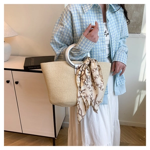 Detail of beige woven straw tote bag with round silver metal handle and patterned silk scarf