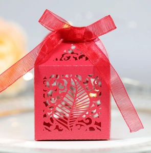 Close-up of red laser-cut wedding favor box with elegant leaf patterns and ribbon