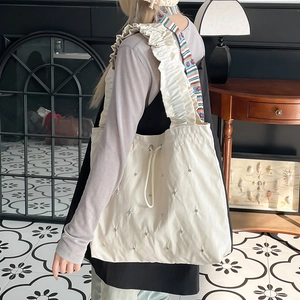 Detail of white nylon tote bag featuring ruffled strap and micro rivet accents