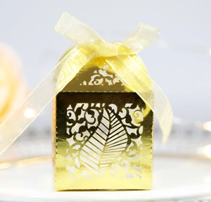 Detail of laser-cut gold wedding favor box with intricate leaf patterns and silk ribbon