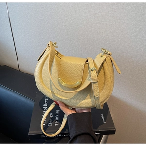 Detail of beige crescent saddle bag with lychee texture and gold metal hardware