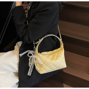 Detail of yellow quilted handbag featuring pearl lace bow charm and smooth gloss finish