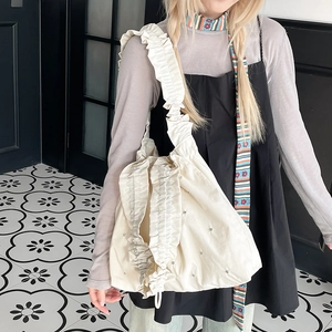 Detail of cream nylon tote bag featuring ruffled strap and delicate beaded embellishments