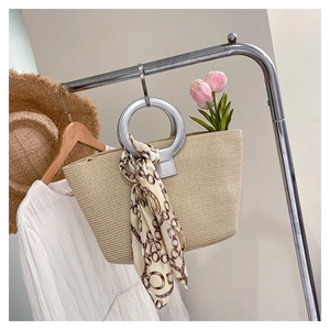 Close-up of beige woven straw tote with silver metal handles and printed silk scarf detail