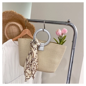Close-up of woven straw tote bag with large silver metal handles and a printed silk scarf