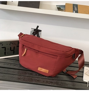 Détail du sac bandoulière en nylon rouge avec patch logo en cuir et sangle réglable