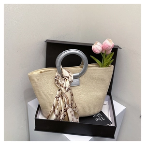 Detail of beige woven tote bag with round silver metal handle and silk scarf decoration