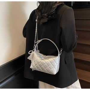Close-up of silver quilted handbag with pearl chains and lace charms on a black blazer