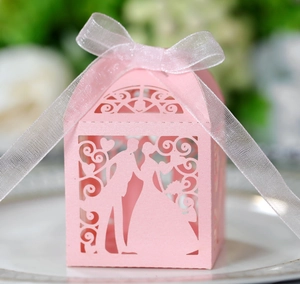 Close-up of pink laser-cut wedding favor box with bride and groom silhouette and ribbon