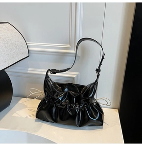 Détail d'un sac plissé en cuir verni noir avec bandoulière réglable et détails froncés