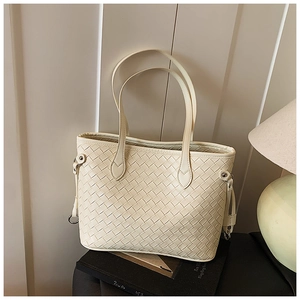 Detail of cream woven tote bag showing premium leather texture and dual handles