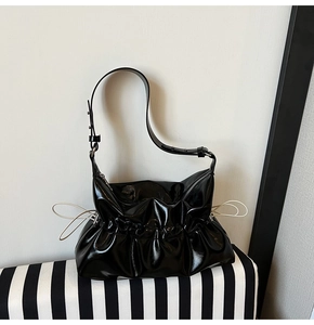 Vue détaillée du sac en cuir verni noir avec design plissé et œillets argentés sur la bandoulière