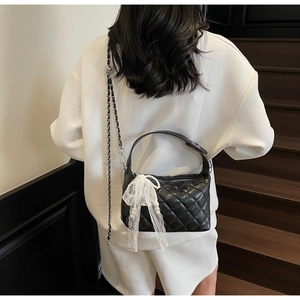 Detail of quilted black hobo bag with white lace bow and pearl charm on leather chain