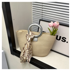 Detail of beige woven tote bag featuring silver ring handles and silk scarf decoration