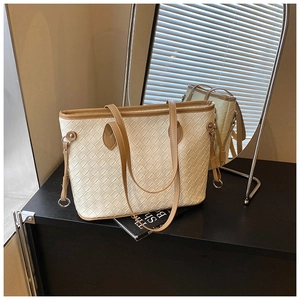 Detail of cream woven tote bag featuring brown leather trim and metallic side buckle