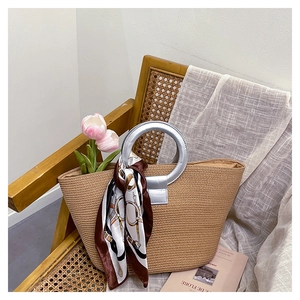 Detail of woven straw tote bag with silver metal ring handles and horse pattern silk scarf