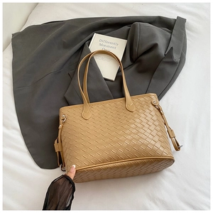 Detailed weave pattern on light brown tote bag set against a grey suit and white bedding