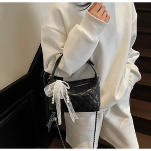 Detail of black quilted leather handbag featuring a white lace bow and pearl charms