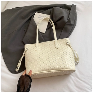 Detailed close-up of woven cream tote bag with refined metal ring and drawstring side accents