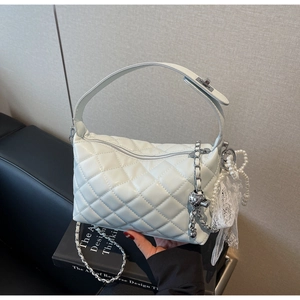 Close-up of quilted white handbag with silver chain strap and pearl bow charm