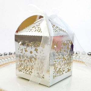 Close-up of silver laser-cut hollow flower candy box with white ribbon on ceramic plate