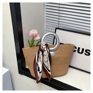 Detail of woven straw tote bag with silver ring handles and equestrian silk scarf