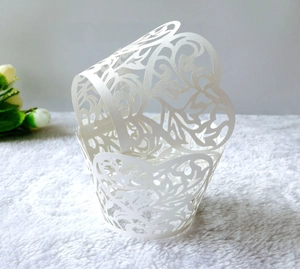 Close-up of white laser-cut cupcake wrapper with intricate floral vine hollow patterns