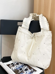Chic beige pleated nylon tote bag with crystal embellishments on a modern chair