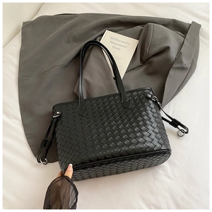 Detail of black woven tote bag with intricate leather texture on grey suit background