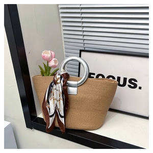 Detail of woven straw tote bag with silver ring handles and stylish printed silk scarf