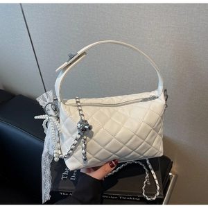 Detail of white quilted crossbody bag with metal chain strap and pearl lace charm