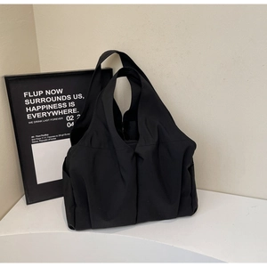 Détail d'un grand sac fourre-tout noir en nylon mat avec côtés plissés sur une surface blanche