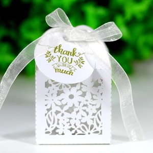 Macro detail of laser-cut floral wedding candy box with white ribbon and thank you tag