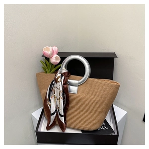 Detail of woven straw tote bag with silver metal handles and a decorative printed silk scarf